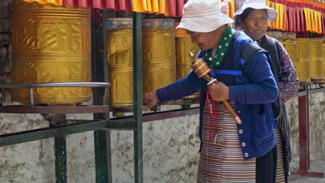 Zwei-ältere-Pilger-Beten-Im-Potala-Palast-Und-Drehen-Die-Goldenen-Gebetsmühlen-In-Lasha