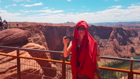 Young-female-tourist-taking-a-Selfie-with-her-phone-from-lookout-point-at-Horseshoe-Bend,-Utah,-USA