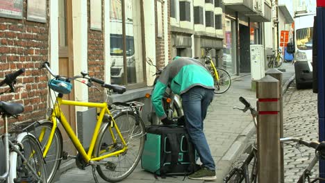 El-Servicio-De-Mensajería-De-Deliveroo-Abre-La-Bolsa-De-Entrega-De-Alimentos-Fuera-De-Un-Edificio-En-Gante,-Bélgica---Plano-General