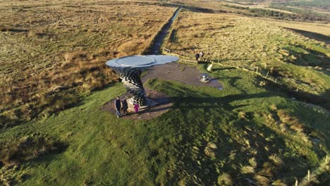 Aerial-singing-ringing-tree-musical-panopticon-sculpture-in-Lancashire-hiking-countryside-orbit-right-passing-tourist-family