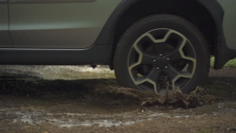 Up-close-Subaru-Crosstrek-driving-through-mud-puddle-on-off-road-trail-in-green-forest-in-the-summer