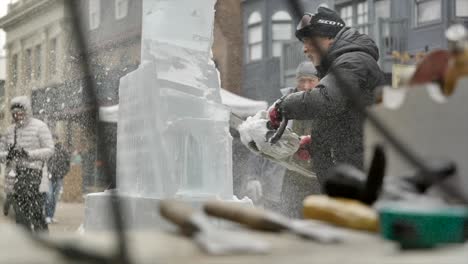 Ice-sculptor-using-chainsaw,-blur-sculpting-tools-on-foreground