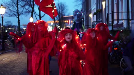 Desfile-De-Rebeldes-Rojos-En-Amsterdam,-Países-Bajos-Al-Anochecer---Activistas-De-La-Rebelión-De-Extinción-Vestidos-De-Rojo-Con-Luces---Cámara-Lenta