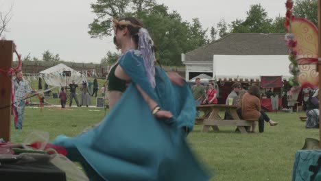 Merchandise-vendor-dances-by-her-stall-foreground-at-a-renaissance-fair,-Philadelphia-Renaissance-Fair,-Fort-Mifflin,-Pennsylvania