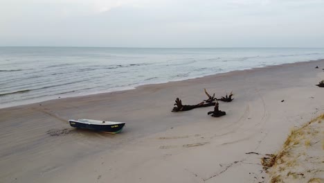 Aerial-view-of-Baltic-sea-coastline-at-Bernati-beach-in-Latvia,-coastal-pine-forest-and-white-dunes,-flying-backwards-over-white-sand-beach-and-fisherman-boat,-wide-angle-establishing-drone-shot