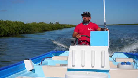 Tiro-Medio,-Hombre-Con-Camisa-Roja-Dirigiendo-El-Volante-Del-Barco-En-El-Mar-De-Adolfo-Lopez-Mateos-Baja-California-Sur,-Méjico,-Vista-Panorámica-Del-Bosque-De-Manglares-En-El-Fondo