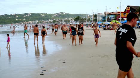 Carro-De-Gente-Caminando-En-La-Arena-Cerca-De-La-Orilla-Del-Mar-En-La-Zona-De-Las-Playas-De-Bombas-Y-Bombinhas,-Brasil