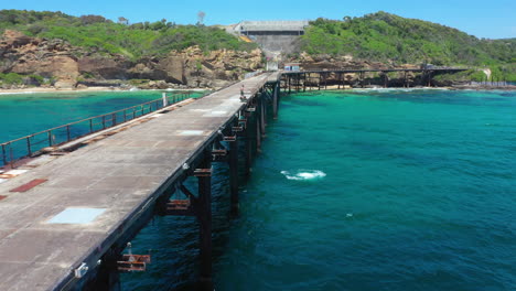 Young-male-jumping-off-abandoned-pier-into-sea-with-friends,-aerial-view