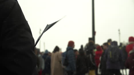 Wide-shot-of-protesters-with-person-holding-Finland-national-flag-in-the-foreground,-flag-waving-the-the-wind