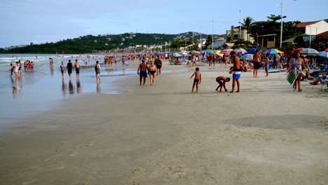 Dolly-in-of-people-having-fun-by-the-sea-and-resting-under-umbrellas-in-Bombas-and-Bombinhas-beaches,-Brazil