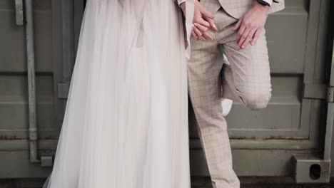 Uprising-shot-of-a-retro-styled-wedding-couple-holding-hands-while-leaning-on-a-grey-container