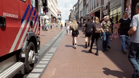 Vista-Lateral-Del-Camión-De-Bomberos-Moviéndose-A-Través-De-La-Multitud-De-Personas,-Zona-Peatonal-Nijmegen