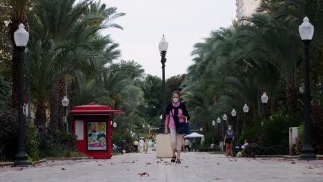 Locked-shot-of-an-ederly-woman-with-hygienic-mask-walking-in-a-pedestrian-area-of-Alicante,-Spain