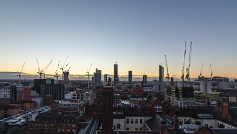 Daylight-fades,-sun-sets,-plane-streaks-across-sky-as-clouds-roll-by-and-construction-cranes-build-new-skyscrapers-in-Manchester,-UK