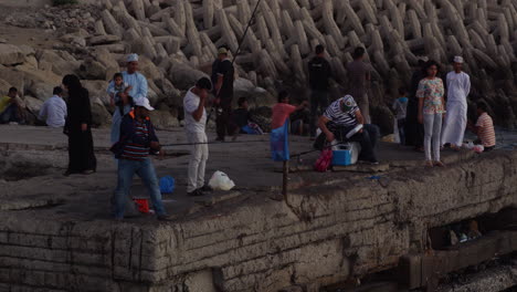 Un-Grupo-Mediano-De-Personas-Pescando-En-Un-Muelle-Al-Atardecer-En-Muscat,-Omán,-Plano-General