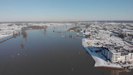 Nuevo-Edificio-De-Apartamentos-De-Lujo-Contemporáneo-En-Un-Paisaje-Urbano-De-Nieve-Brillante-En-La-Orilla-Del-Río-Ijssel-En-Un-Paisaje-Blanco-Invernal-Cubierto-De-Nieve-Con-Un-Alto-Nivel-De-Agua-Estacional-Que-Llena-Las-Llanuras-Aluviales