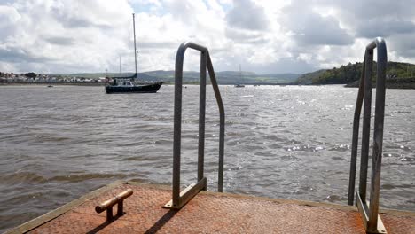 Metal-jetty-ladder-handles-on-idyllic-swimming-pier-with-picturesque-boats-on-coastline-horizon