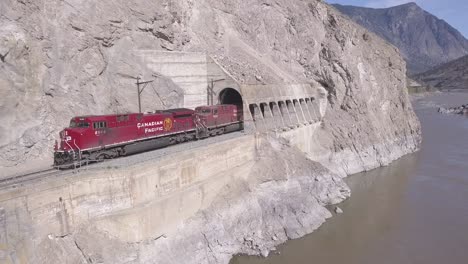 Cp-Güterzug-Mit-Offenen-Schüttgutwagen-Fährt-Aus-Dem-Tunnel-Am-Flussufer-Hervor