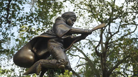 Ikonische-Statue-Von-Harry-Potter,-Die-Auf-Einem-Besen-Am-Leicester-Square-In-London-Fliegt,-Mit-Wehenden-Bäumen-Im-Hintergrund