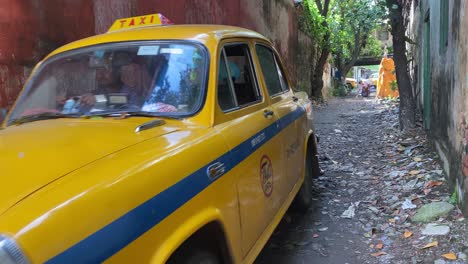 Gelbes-Taxi-Kommt-An-Einem-Frühen-Samstagmorgen-An-Einem-Sonnigen-Tag-Aus-Der-Garage-Mit-Roten-Wänden-Durch-Die-Straße-Von-Kalkutta