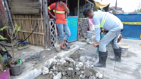 Foremen-wearing-safety-reflective-vests-use-their-shovel-and-demolition-hammer-to-perform-deep-excavation-beside-the-road-and-gutter-for-installing-new-water-piping-from-the-main-water-line