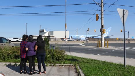 Three-girls-standing-across-the-street-looking-at-a-plane