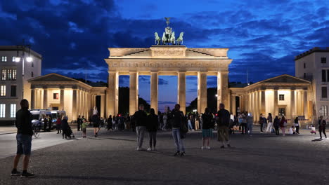 Berlín,-Alemania---Alrededor-De-Agosto-De-2021:-Grupo-De-Personas-Frente-A-La-Puerta-De-Brandeburgo-Iluminada-Por-La-Noche,-Punto-De-Referencia-De-La-Ciudad-De-Estilo-Neoclásico