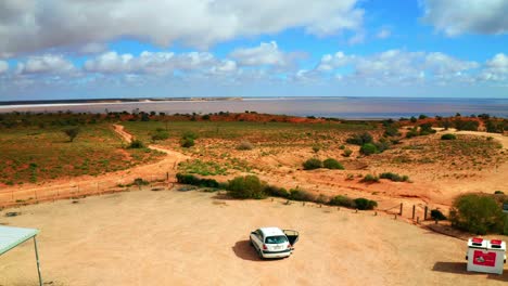 Vista-Aérea-De-Un-Automóvil-En-Un-Estacionamiento-Aeria-En-El-Interior-Australiano-Con-Un-Lago-En-El-Fondo---Victoria,-Australia