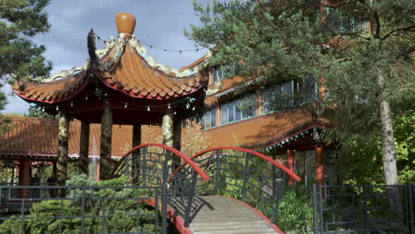 Un-Puente-Arqueado-Que-Cruza-Un-Estanque-Para-Unirse-A-Un-Pabellón-De-Estilo-Asiático-En-Medio-De-Un-Jardín-De-Lotos,-Un-Jardín-Tranquilo-De-Un-Lugar-De-Celebración-De-Bodas-De-Temática-Oriental,-Excelencia,-Midlands,-Inglaterra