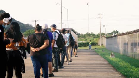 A-line-of-commuters-waiting-patiently-at-the-bus-stop-outside-Albrook-Metro-station,-everyone-wearing-protective-facemasks-and-practicing-social-distancing