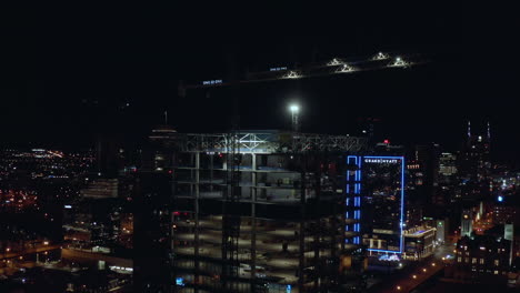 Antena-De-La-Ciudad-Nocturna-De-La-Torre-Del-Edificio-En-Construcción-Con-Grúas-En-La-Parte-Superior,-4k