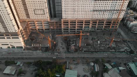 Drone-flying-backwards-with-camera-tilt-up-shows-a-building-under-construction-and-a-busy-road-with-many-motorists