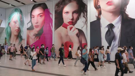 Hundreds-of-commuters-wearing-protective-masks-walk-past-through-a-large-commercial-advertisement-at-Hong-Kong-MTR-subway-station-early-morning-in-Central-district,-Hong-Kong