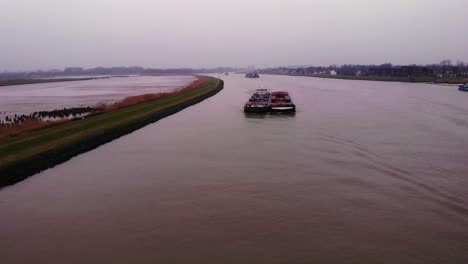 Vuelo-Aéreo-Sobre-El-Buque-De-Carga-Maas-Emparejado-Con-Otro-Que-Transportaba-Contenedores-En-El-Río-Noord-Junto-A-Crezeepolder-En-Una-Tarde-Nublada