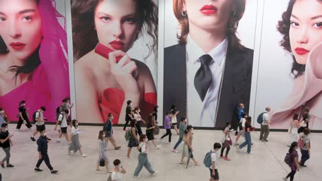 Large-crowds-of-people-walk-past-a-large-commercial-advertisement-banner-at-Hong-Kong-MTR-subway-station-early-morning-in-Central-district,-Hong-Kong