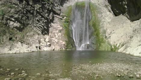 Young-trekker-sitting-over-a-stone-in-a-mountain-amazing-landscape-with-a-pristine-waterfall