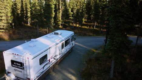 Aerial,-rising,-drone-shot,-of-a-camper-van,-driving-on-a-road-surrounded-by-spruce-forest,-near-Johnson-lake,-in-Kenai-Peninsula-of-Alaska,-United-states-of-america