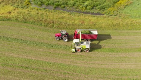 4K-Luftaufnahme-Mit-Schwenk-Nach-Links-Von-Einem-Mähdrescher,-Der-Heu-In-Einen-Traktor-Und-Einen-Wagen-Erntet