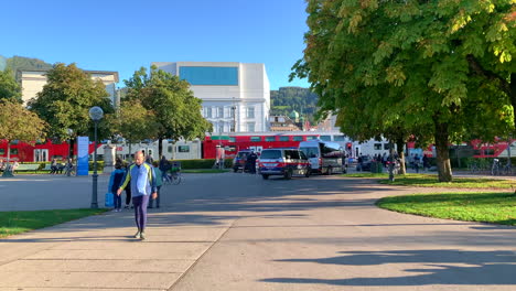 Austrian-OBB-Train-passing-through-a-railway-with-police-car,-building-and-crowds-walking-and-trees-in-the-background