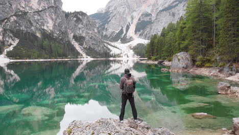 Un-Dron-Revelador-Hacia-Atrás-De-Un-Modelo-Masculino-Parado-En-Una-Roca-Con-Vista-Al-Lago-Braies-En-Los-Dolomitas,-Italia