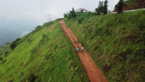 Drone-view-of-Vietnamese-locals-travelling-along-a-dirt-road-by-foot,-carrying-packs-on-their-back