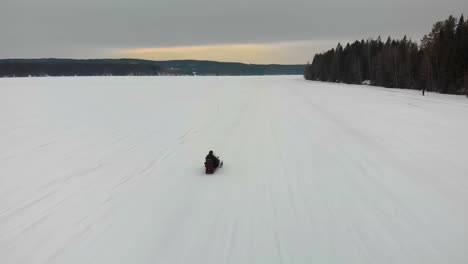 Tracking-aerial-shot-of-a-man-driving-his-snowmobile-on-Indalsalven-in-Timra,-Sundsvall,-Sweden