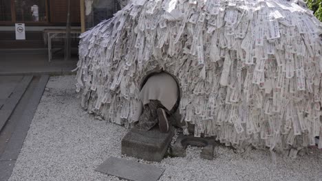 Japan---A-lady-is-doing-a-worship-ritual-entering-a-tiny-circled-hole-decorated-with-white-paper-with-Japanese-writings-in-a-Shinto-Temple---Close-up