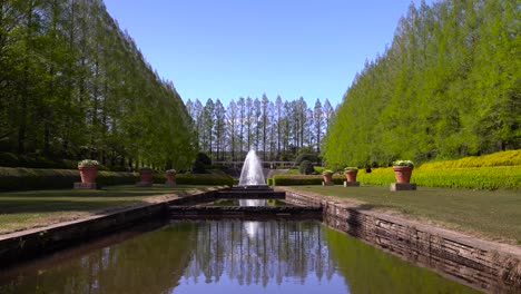 El-Hermoso-Paisaje-De-Un-Parque-Público-Lleno-De-árboles-Verdes-Y-Una-Fuente-De-Agua-Situada-En-El-Centro-En-Un-Cielo-Azul-Soleado---Tiro-Amplio