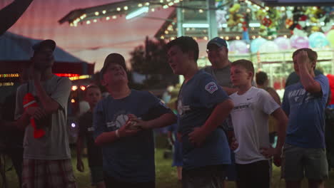 Young-boy-with-friends-playing-speed-pitch-game-at-carnival-at-dusk,-Slow-Motion