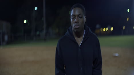 African-American-Teen-Walks-on-Baseball-Field-at-Night,-Front-Medium