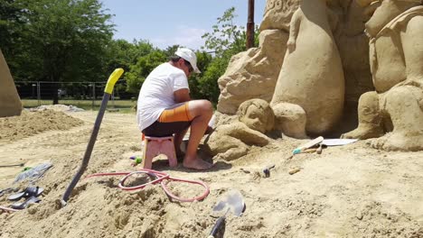 Hombre-Trabajando-En-Una-Figura-De-Arena-De-Un-Bebé-Para-El-Festival-De-Arena-En-Burgas,-Bulgaria---Vista-Lateral,-Tiro-De-Acercamiento