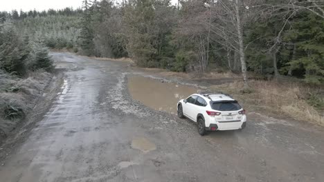 Un-Subaru-Crosstrek-Blanco-Solitario-Se-Sumerge-En-Un-Charco-De-Lodo-Profundo,-Antena-En-Cámara-Lenta,-Editorial-Ilustrativa