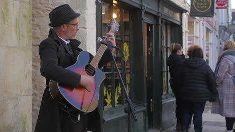 A-busker-playing-music-on-the-street-of-Truro,-England,-entertaining-the-people---Wide-shot