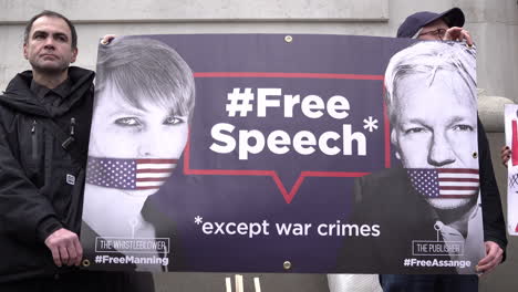 Protestors-stand-holding-a-banner-with-a-picture-of-Julian-Assange-and-Chelsea-Manning-on-that-says-#FreeSpeech-except-war-crimes-on-a-protest-calling-to-stop-the-extradition-of-the-Wikileaks-founder